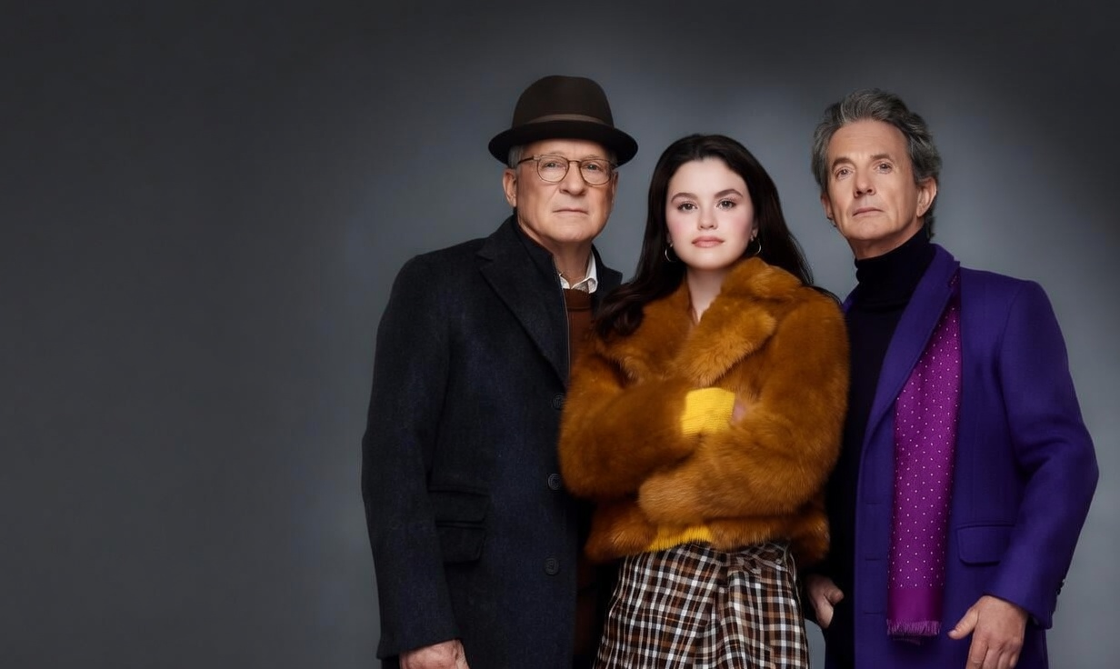 Promotional image for Only Murders in the Building television series, featuring actors Steve Martin in an overcoat and hat, Selena Gomez in a yellow fur jacket and plaid skirt, and Martin Short in a purple coat with a polka-dot scarf, all side-by-side against a dark backdrop with the show's title in bold white text.