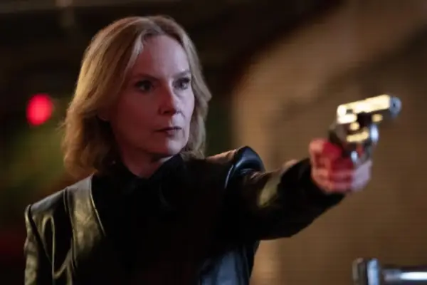 Jan pointing a gun with a serious expression in a tense, dimly lit scene from Only Murders in the Building.